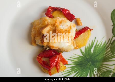 Überzug aus weißem Fisch, lackiert mit gerösteten Eiern, begleitet von roten Paprika, Kartoffeln und Knoblauch auf einem Teller mit abstrakter Dekoration. Angeln und heilen Stockfoto