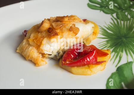 Überzug von Kabeljau mit gerösteten Eiern, begleitet von roten Paprika, Kartoffeln und Knoblauch auf einem Teller mit abstrakter Dekoration. Fisch und Gesundheit. Stockfoto