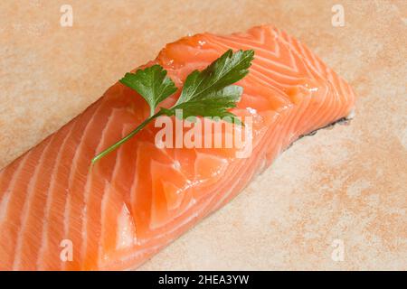 Nahaufnahme eines Zweig Petersilie auf einem frischen rohen Lachsfilet auf einem abstrakten künstlerischen Hintergrund mit einer Textur in Pastellfarben. Gesundes Essen und Fisch Stockfoto