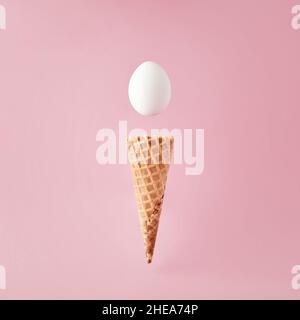 Eiskegel mit fliegendem weißen Ei auf rosa Hintergrund. Minimales Essen oder Osterkonzept. Stockfoto