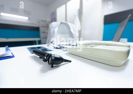 Helle leere Arztpraxis mit professionellen medizinischen Instrumenten für die klinische Untersuchung ausgestattet. Krankenhauszimmer mit niemand darin, der Otoskop und Festnetz auf dem Schreibtisch hatte. Medizinkonzept Stockfoto