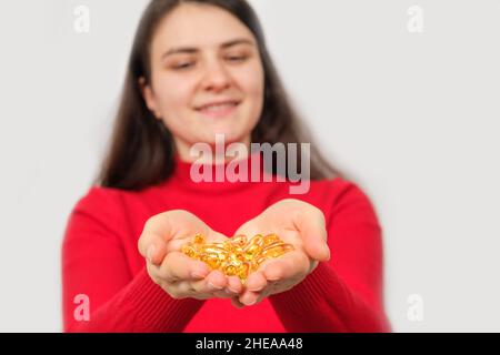 Eine lächelnde Frau hält in ihren Handflächen eine Handvoll Kapseln Fischöl, Omega 3. Stockfoto