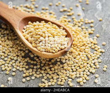 Roher Couscous in Holzlöffel auf grauem Betongrund Stockfoto