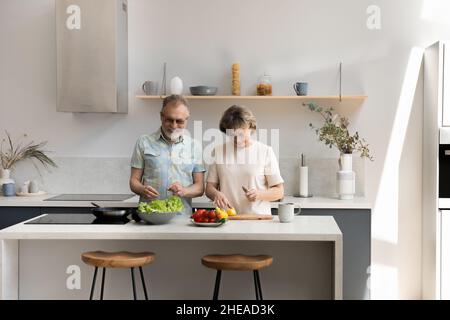 Glückliches Paar mittleren Alters kocht zusammen in der Küche. Stockfoto