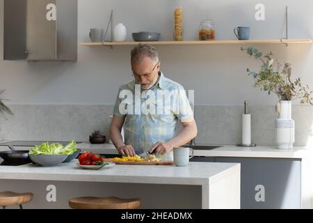 Glücklicher älterer Mann mittleren Alters, der in der Küche kocht. Stockfoto