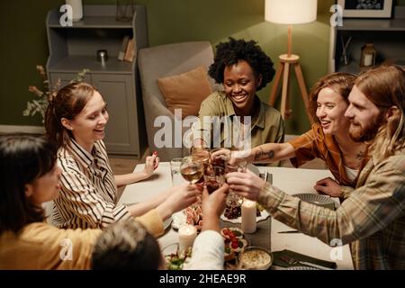 Eine Gruppe von glücklichen Freunden, die am Esstisch mit Getränken toasten und gemeinsam den Urlaub feiern Stockfoto