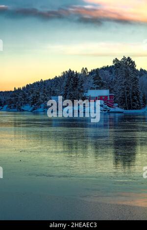 Eis bedeckt Vollsfjord und bunten Himmel spiegelt sich im Eis. Winterlandschaft mit Inseln, Hütten, Meer, schneebedeckten Felsen, blauem Himmel, Reflexion bei Sonnenuntergang. , Stockfoto
