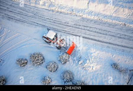 Schneeräumung mit rotem Traktor auf der Straße. SUNY Wintertag, Drone Blick von oben. Antenne. Blick von oben. Stockfoto