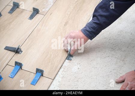 Contractor Hände Verlegung keramische Holz-Effekt Fliesen mit Fliesenlegern. Stockfoto