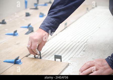 Arbeiter Hände Verlegung keramische Holz-Effekt Fliesen mit Fliesenlegern. Stockfoto