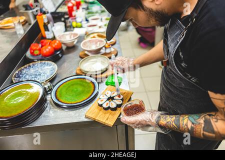 Die männlichen Köche bereiten Sushi in der Restaurantküche zu. Der Koch schmückt die Brötchen mit Wasabi Stockfoto