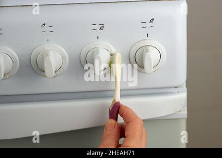 Weibliche Hand wäscht die Wasserhähne des weißen Gasofens mit einer Zahnbürste. Eine ungewöhnliche Art der Hausreinigung Stockfoto