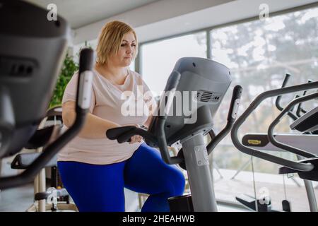 Glückliche, übergewichtige Frau mit mittlerem Erwachsenen, die im Fitnessstudio auf dem Stepper trainiert Stockfoto