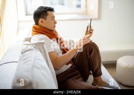 Kranker asiatischer Mann hustet und Smartphone benutzt Stockfoto