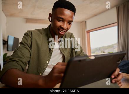 Junge Erwachsene schwarze männliche Schreiben mit Stift auf elektronischem Tablet während der Arbeit aus der Ferne von modernen zu Hause Stockfoto