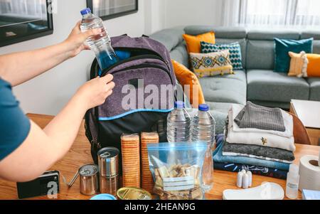 Frau, die eine Wasserflasche zur Vorbereitung eines Notfallrucksacks legt Stockfoto