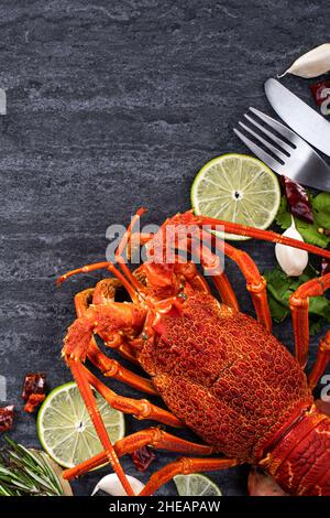 Blick von oben auf gekochten gekochten Hummer, köstliches Abendessen mit Fisch und Meeresfrüchten, mit Messer und Gabel auf schwarzem Schiefergrund für den Valentinstag. Stockfoto