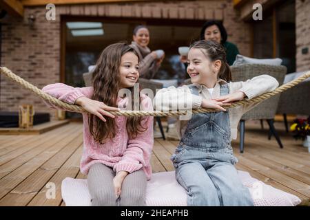 Zwei glückliche Schwestern mit Mutter und Großmutter sitzen im Herbst draußen auf der Terrasse. Stockfoto