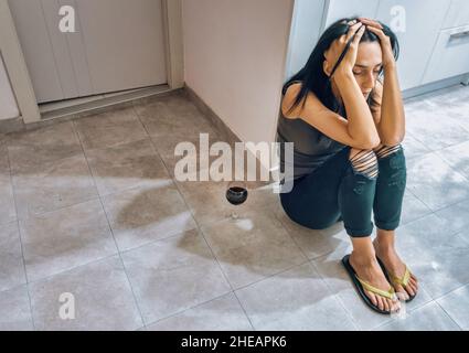 Junge attraktive kaukasische Frau sitzt auf der Küche Florr müde mit den Händen auf dem Kopf und ein volles Glas Wein. Stockfoto