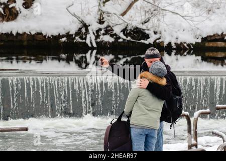 Liebe überall. Küssendes Paar, das Selfie in der Nähe eines Wasserfalls nimmt. Junger Mann und Frau zusammen. Stockfoto