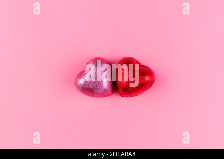 Konzept vom 14. februar oder Valentinstag. Schokoladenbonbons Herzen in rosa und roten Umhüllungen. Rosa Hintergrund. Speicherplatz kopieren. Stockfoto