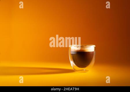 Frisch gebrühter cremiger Espresso in einer Tasse mit Glas, isoliert auf gelbem Hintergrund, Nahaufnahme mit Kopierraum Stockfoto