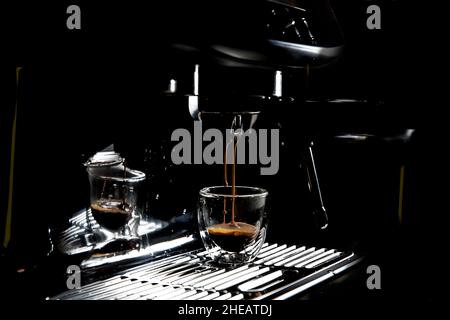 Dunkle Kaffeetropfen tropfen in einer Espressotasse aus transparentem Glas auf einer manuellen Espressomaschine mit Kopierfläche, Nahaufnahme Stockfoto