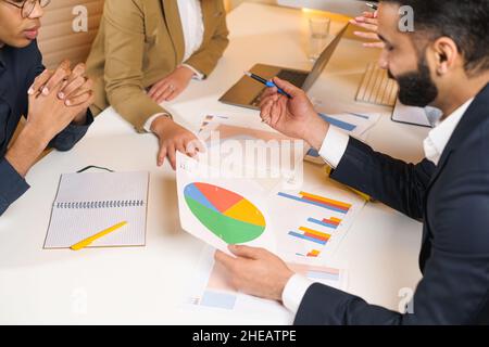 Eine Gruppe junger Geschäftsleute, die in einem großen Coworking-Büro zusammenarbeiten. Marketingabteilung diskutiert Produktplan. Brünette Frau zeigt etwas zu Kollegen. Neues Startup-Firmenkonzept Stockfoto