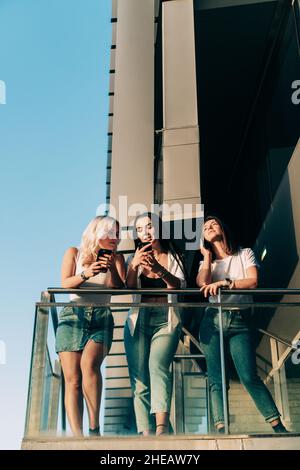 Drei Freundinnen, die ihre Handys benutzen, während sie sich im Freien zusammen aufhalten. Stockfoto