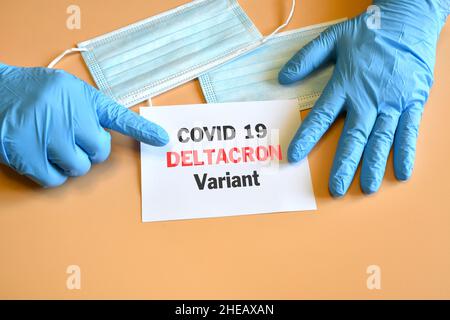 Covid-19 neue Deltacron-Variante. Die Hände des Arztes in blauen Handschuhen halten ein weißes Papier mit der Aufschrift 'Covid-19 Deltacron Variant'. Stockfoto