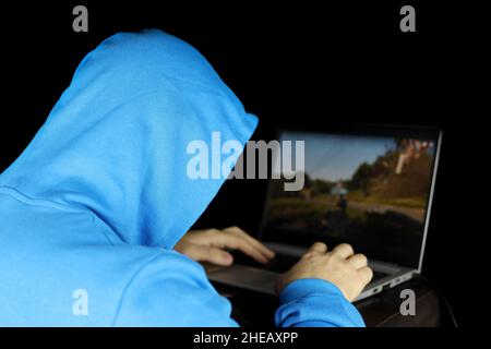 Kerl in blauem Hoodie, der ein Computerspiel auf einem Laptop spielt. Konzept der Spielsucht, Freizeit zu Hause Stockfoto