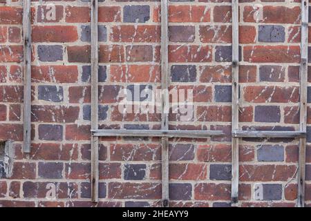 Nahaufnahme einer Ziegelwand mit einem zerbrochenen Gitter und alten Wurzeln. Stockfoto