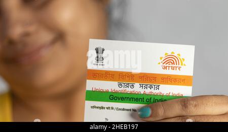 Birbhum, Westbengalen / Indien - 21st. Dezember 2021: Selektiver Fokus auf die Aadhaar-Karte, die von einer jungen Inderin mit lächelndem Gesicht in der Hand gehalten wird Stockfoto