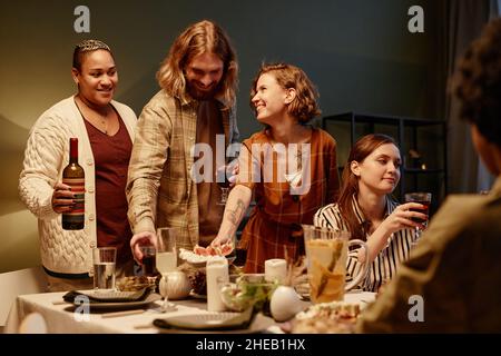 Gruppe von glücklichen jungen Freunden, die sich während der Heimparty am Tisch amüsieren Stockfoto