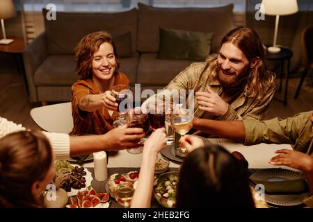 Eine Gruppe von glücklichen Freunden, die mit einem Glas Rotwein toasten und sich gegenseitig am Esstisch zu Hause gratulierten Stockfoto