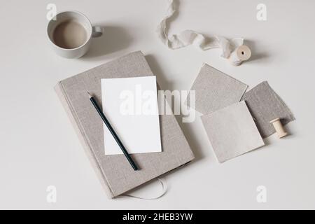 Basteln Sie Stillleben. Beigefarbene Leinenmuster und Seidenband auf beigem Tischhintergrund isoliert. Tasse Kaffee. Leeres Grußkartenmockup, Bleistift auf Stockfoto