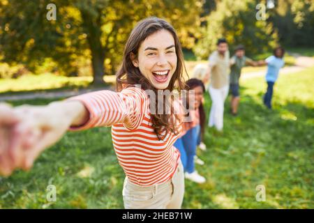 Lachende junge Frau steht bei einem Teambuilding-Spiel Hand in Hand mit Freunden Stockfoto