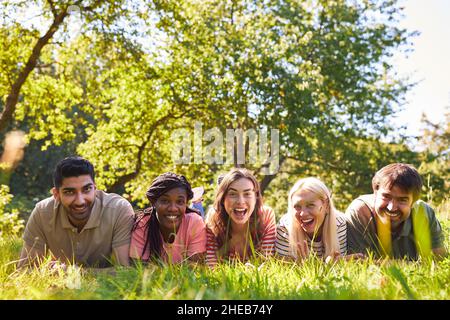 Multikulturelle Gruppe junger Menschen, die im Sommer lachend auf einer Wiese liegen Stockfoto