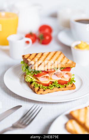 Toast-Sandwich mit gouda-Käse und putenschinken gefüllt mit Tomaten und Salat auf einem hellen Hintergrund mit Zutaten in verschwommenem Hintergrund. Serviert wi Stockfoto