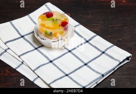 Kuchen mit Gelee, Kiwi, Kirschen und Mango auf dem Tisch. Leckeres Mini-Dessert auf einem hölzernen Hintergrund, Nahaufnahme. Stockfoto