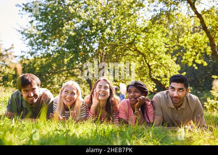 Eine Gruppe von Freunden, die im Sommer zusammen auf der Wiese lachend liegen Stockfoto