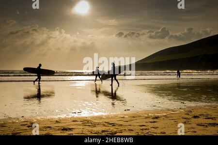 Atmosphärisch breite Aufnahme von 3 Surfers, die gegen die Sonne mit Strandreflexionen am Strand von Saunton Sands im Norden von Devon UK gedreht wurden. Stockfoto