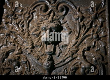 Ein dekorativer, dekorativer Löwenkopf mit ansetzenden Augen steht vor Beginn der Renovierungsarbeiten an einem antiken gusseisernen Kamin in einem alten Haus. Stockfoto