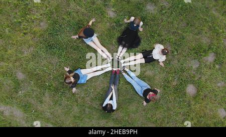 Freunde sitzen auf dem Gras, ihre Beine sind in einem Kreis zusammengefügt. Stockfoto