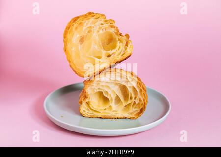 Croissant in zwei Stücke geschnitten isoliert auf violettem Hintergrund. Einfaches und elegantes Konzept. Stockfoto