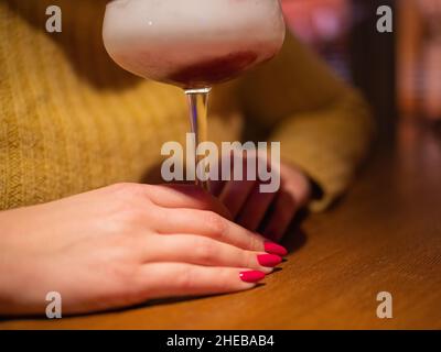 Coupé-Glas mit rotem Cocktail. Handhaltenden Minzzweig. Frischer und duftender Kleeblatt-Club. Entspannen Sie sich und genießen Sie einen Cocktail Stockfoto