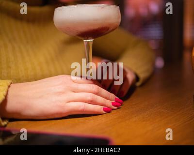 Coupé-Glas mit rotem Cocktail. Handhaltenden Minzzweig. Frischer und duftender Kleeblatt-Club. Entspannen Sie sich und genießen Sie einen Cocktail Stockfoto