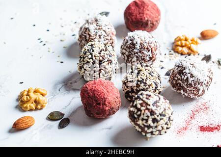 Rohes veganes Dessert. Energiebälle. Trüffel aus Nüssen, Samen, Kakao, Datteln und verschiedenen Superfood-Pulvern, weißer Marmorhintergrund. Stockfoto