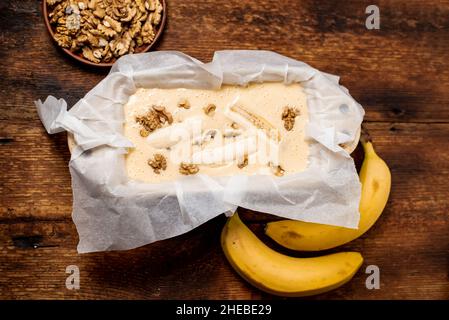 Ungekochte Teig Bananenbrot in der Form. Kochen. Holzhintergrund. Blick von oben. Süßes, vegetarisches Essen. Stockfoto