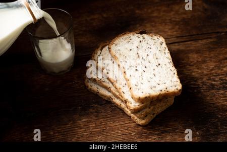 Brotstücke mit Samen und Milch werden in ein Glas gegossen. Dunkler Holzhintergrund. Frühstück am Morgen. Gesunde Ernährung. Stockfoto